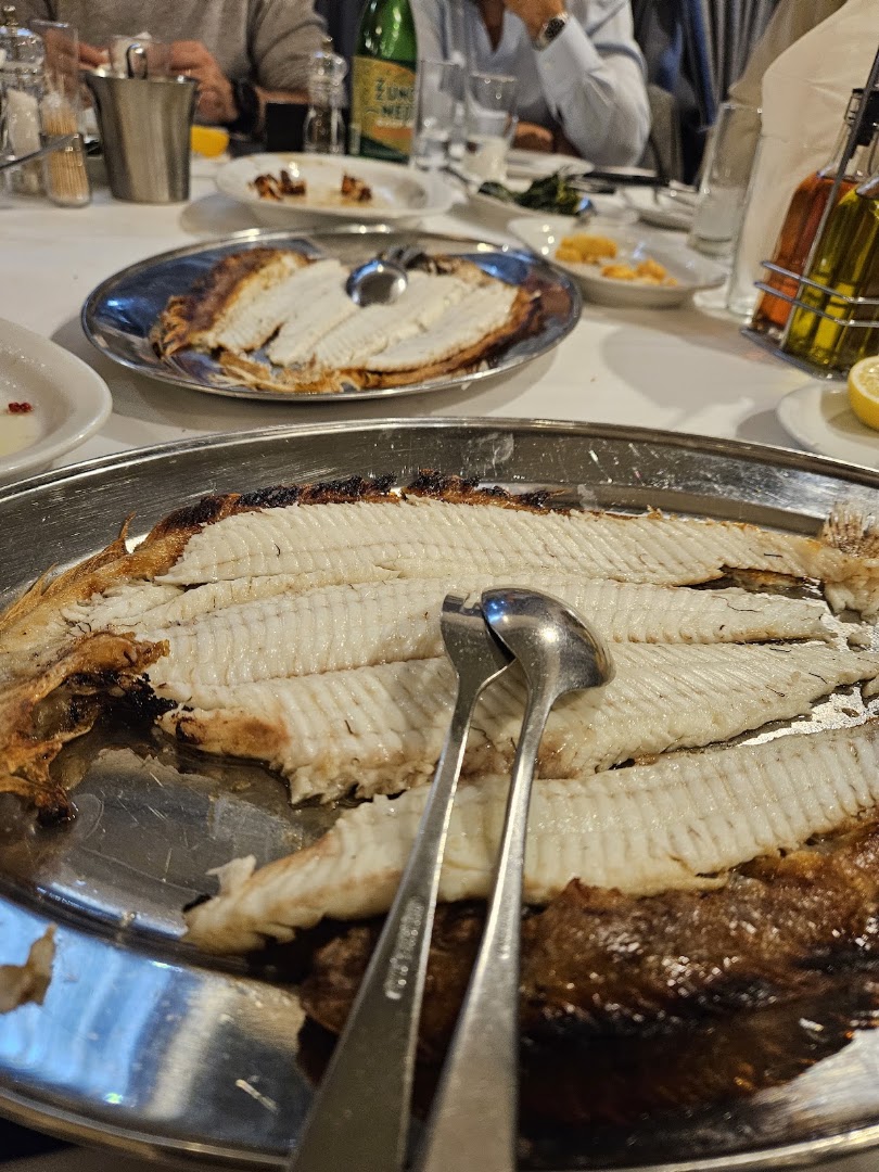Παρέες γύρω από τραπέζια σε εξωτερικό χώρο ταβέρνας με φαγητό και ποτά.